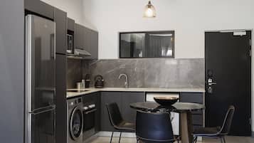 Una cocina moderna con lavadora y secadora integradas, una mesa comedor negra con sillas y un ventanal sobre el fregadero.