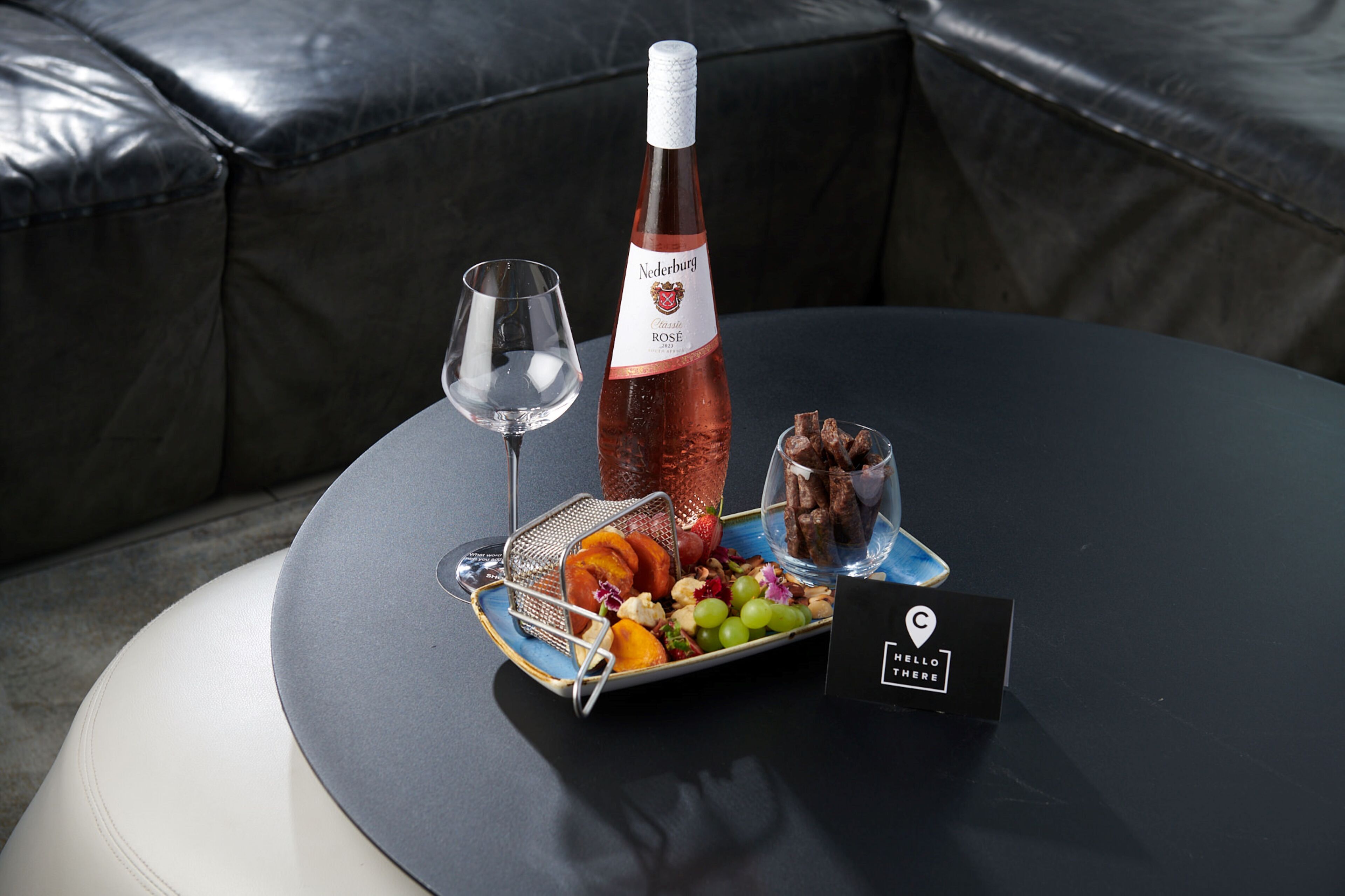 Ein Tisch mit einer Weinflasche, einem Glas und einer Platte mit Obst und Pralinen.