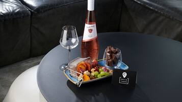 Ein Tisch mit einer Weinflasche, einem Glas und einer Platte mit Obst und Pralinen.