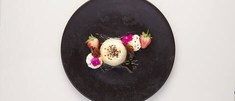 Un plato negro redondo con un postre de fresas y una flor.
