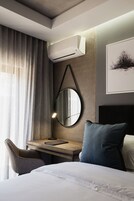 Quarto de hotel moderno com uma cama, uma escrivaninha com cadeira, um espelho redondo e um aparelho de ar condicionado.