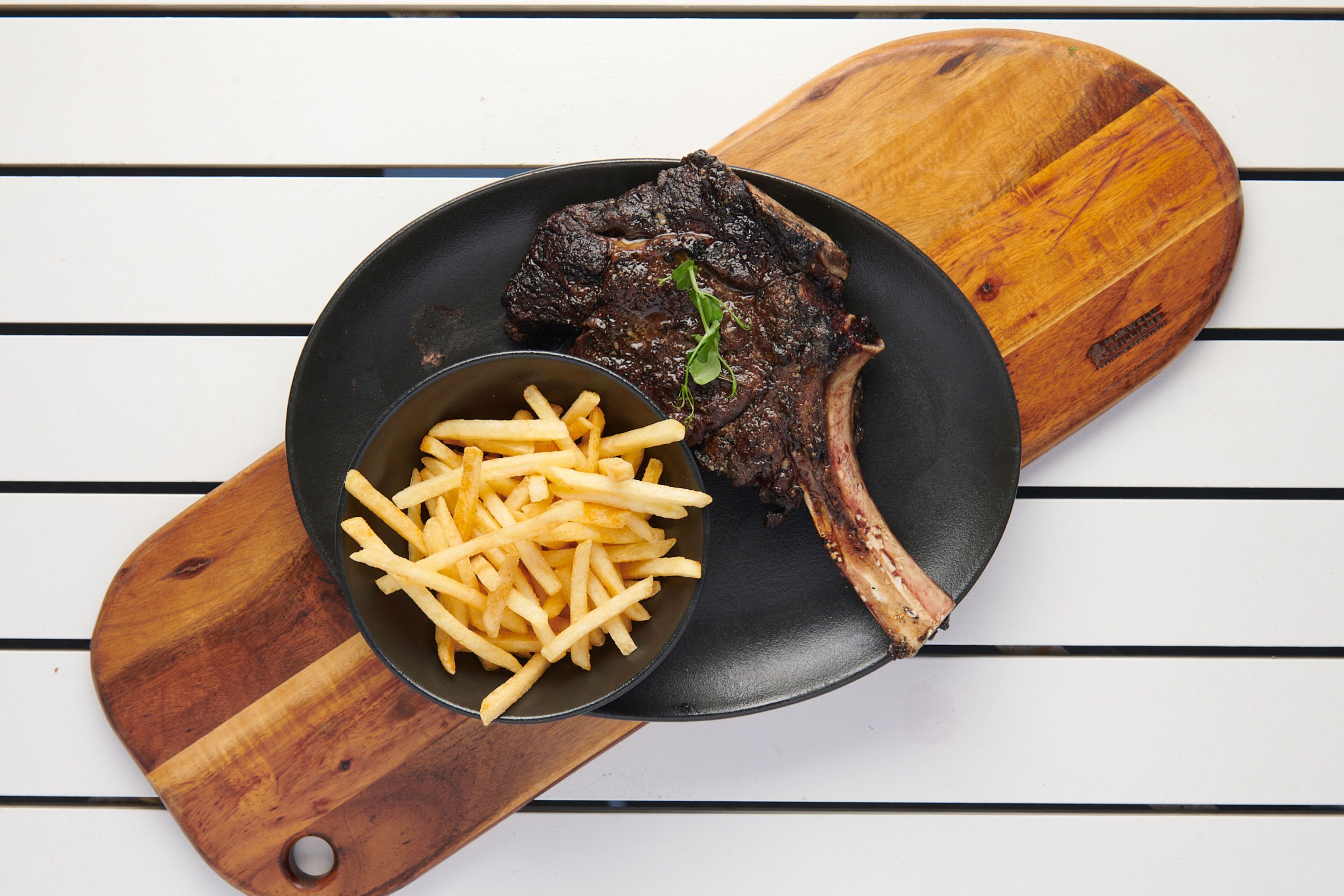 A steak with fries on a black plate, placed on a wooden board.