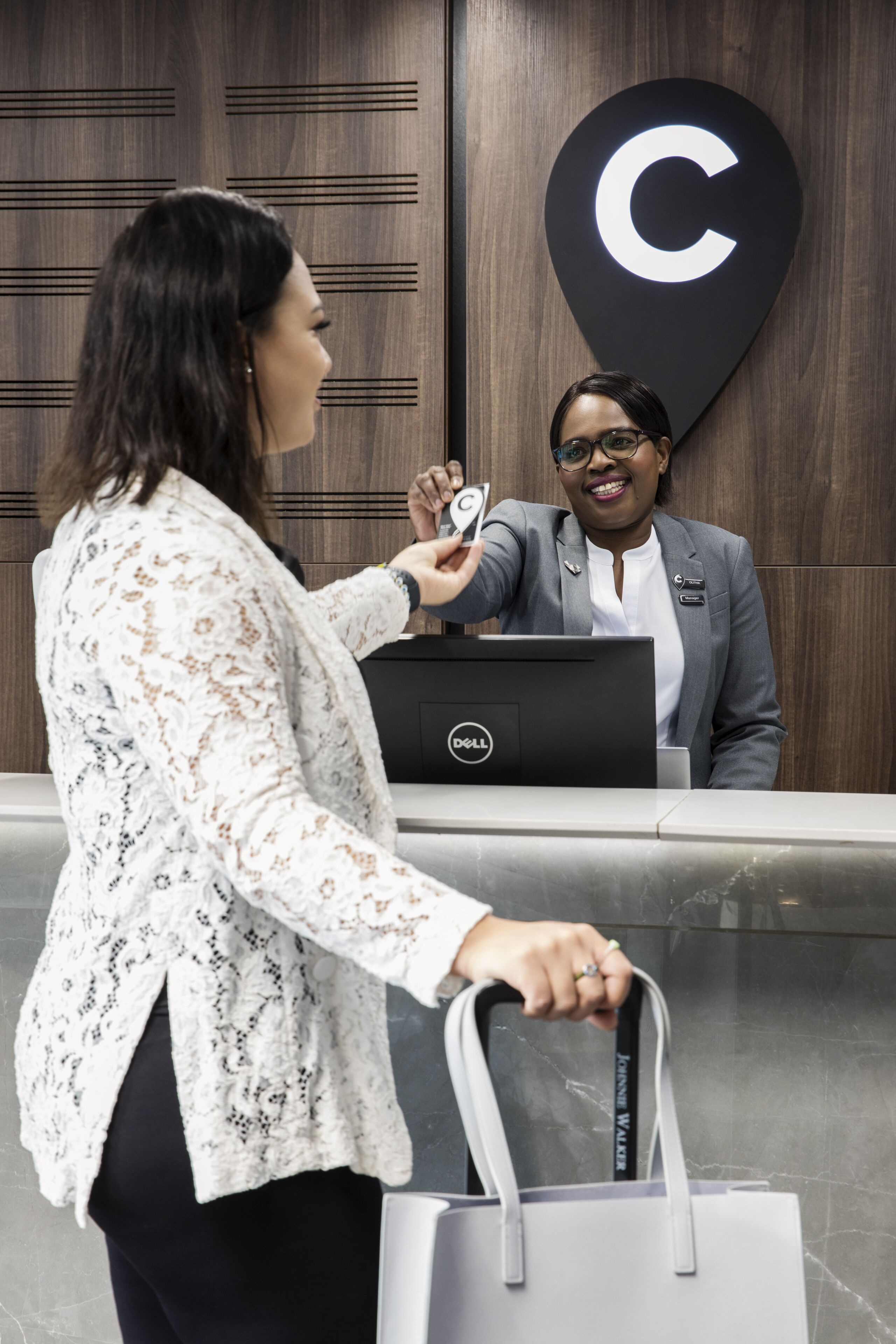 A reception desk with a large 'C' sign, a Dell laptop, and a person holding a card.