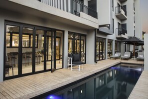 A modern hotel with a pool area, outdoor seating, and a view of the interior dining space. - The Capital Melrose (Johannesburg)