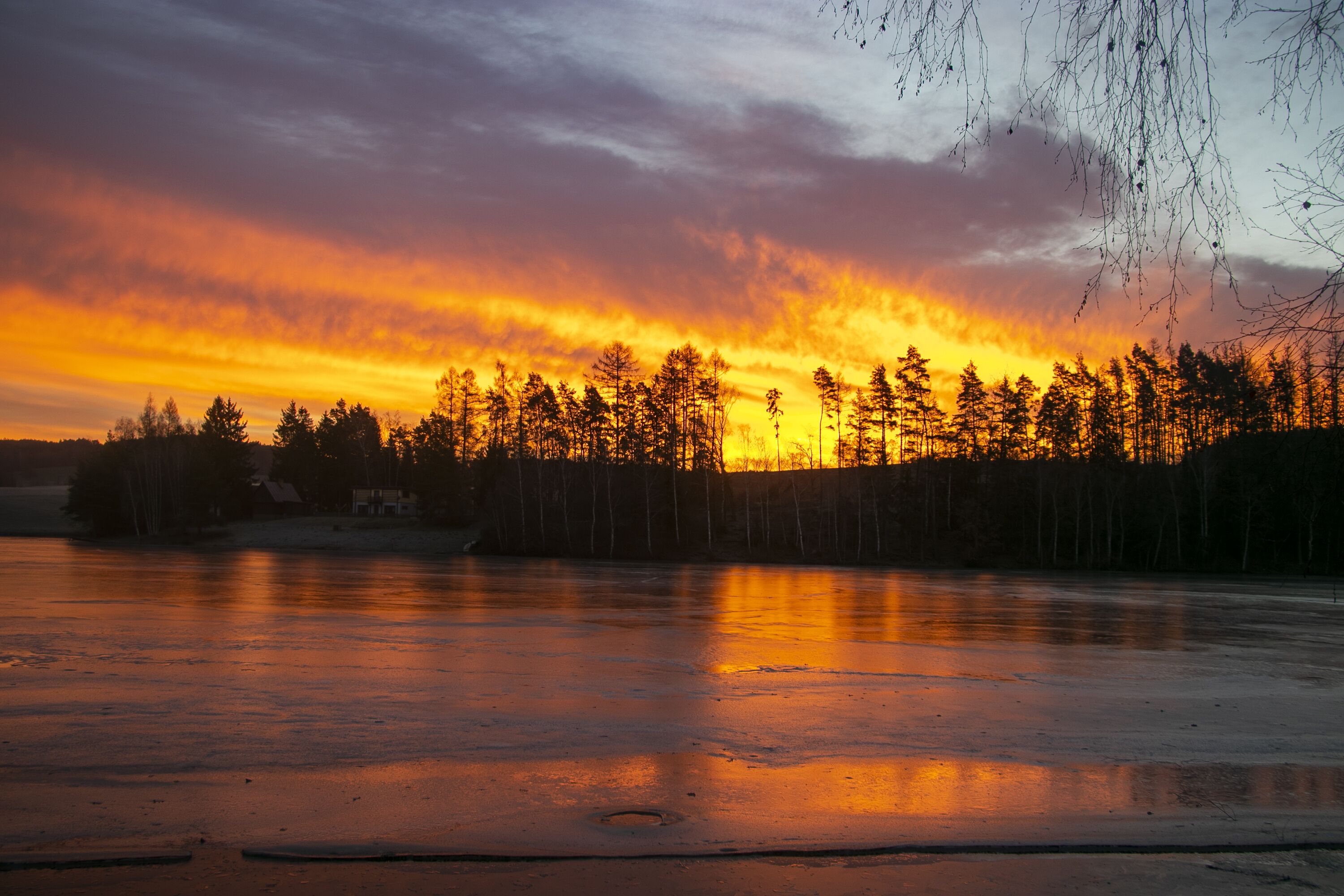Un lac gelé au coucher du soleil, avec des arbres se découpant en silhouette sur un ciel aux couleurs vives.