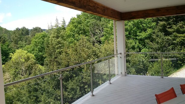 Varanda com guarda-corpo de vidro e vista para uma encosta arborizada.