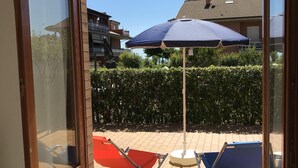 Blick durch eine Glastür auf eine Terrasse mit zwei Klappstühlen und einem blauen Sonnenschirm.