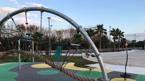 Ein Spielplatz mit einer Taustrafer, einer grünen Kletterkonstruktion und einem gelben, kreisförmigen Bereich.