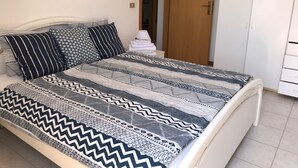 Ein ordentlich bezogenes Bett mit gemusterten Betttextilien, ein gerahmtes Bild an der Wand und ein Schrank mit Schubladen.