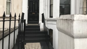 Una escalera conduce a una puerta negra con el número 19, flanqueada por paredes blancas y una barandilla de metal negro.