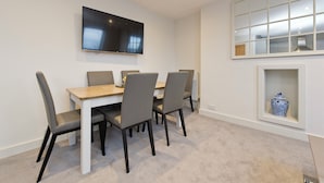 Un comedor con una mesa y cuatro sillas, un televisor de pantalla plana en la pared y un ventanal con un jarrón decorativo.