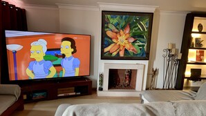 A living room with a flat-screen TV, a fireplace, and a painting. - Seazimbra - Luxury Apartment (Sesimbra)