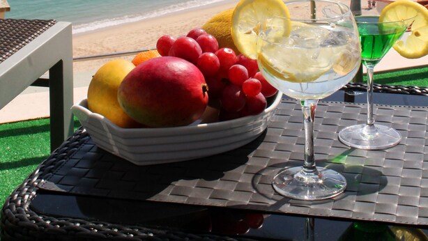 A table with a fruit bowl and two drinks, overlooking a beach and water. - Seazimbra - Luxury Apartment (Sesimbra)