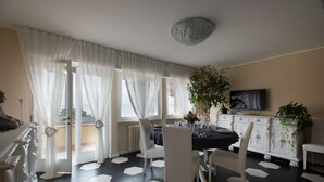 Un comedor con suelo de baldosas blanco y negro, sillas blancas, una mesa redonda y un mueble blanco con televisor.