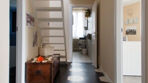 Un pasillo con suelo de baldosas hexagonales blanco y negro, un aparador de madera, una cesta de mimbre y una escalera blanca.