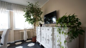 Una habitación con un aparador blanco ornamentado, una planta en maceta, un televisor de pantalla plana y una silla.