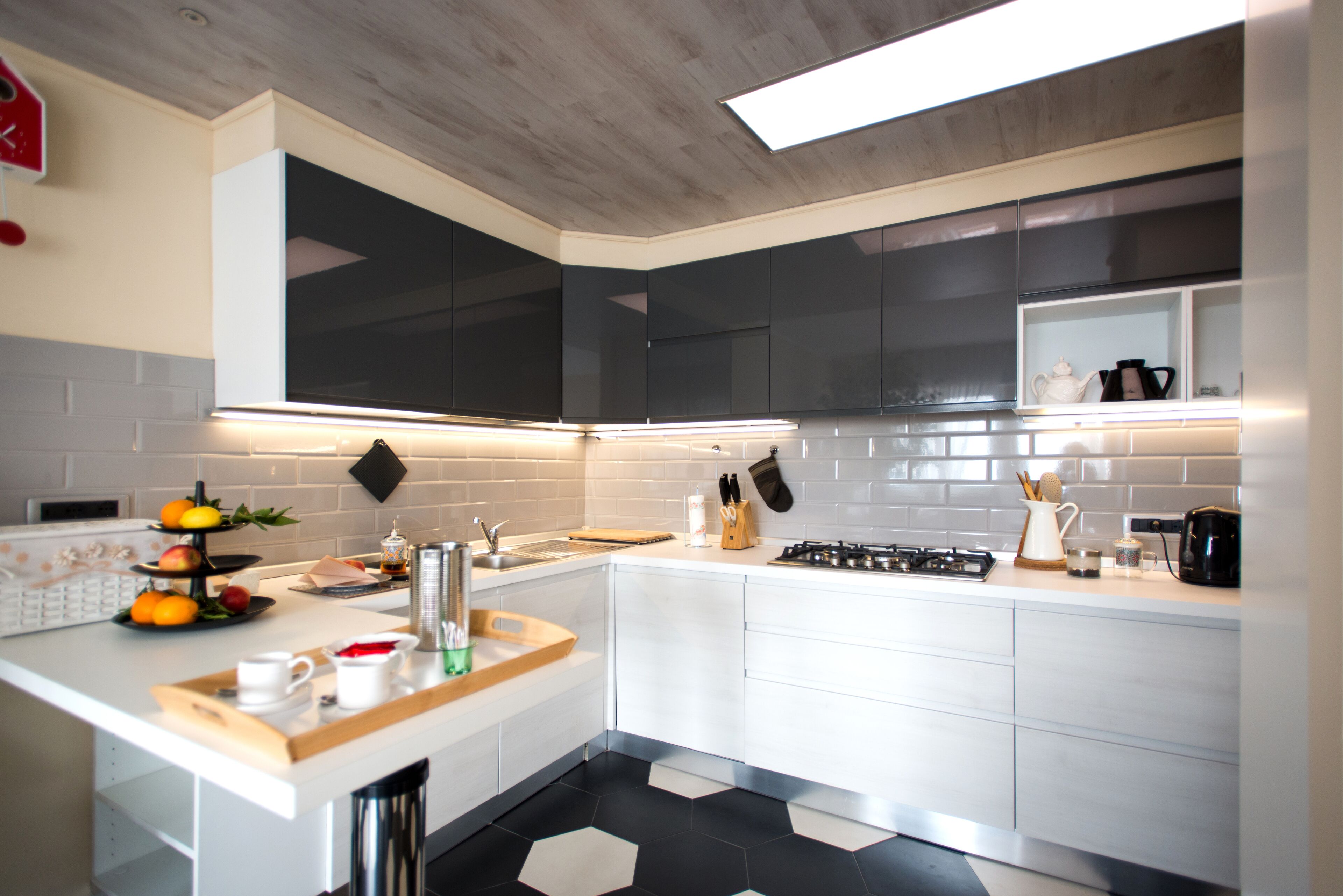 A modern kitchen with white cabinets, a black and white tiled backsplash, a stainless steel sink, and a gas stove.
