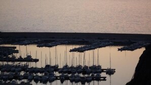 Ein Yachthafen bei Sonnenuntergang mit vertäuten Booten, ruhigem Wasser und Bergen in der Ferne.