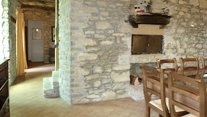 Un interior rústico de piedra con chimenea, sillas de madera y suelo de baldosas.