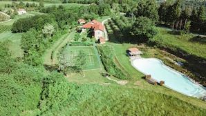 Vista aérea de una propiedad con cancha de tenis, piscina y follaje circundante.