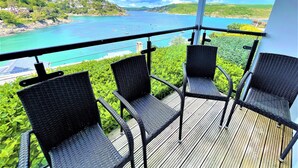 Un balcon agrémenté de fauteuils en osier, donnant sur une mer turquoise et un paysage verdoyant.