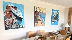 Un espace de salle à manger moderne avec une table en verre, des chaises en bois et trois tableaux sur le thème de la mer accrochés au mur.