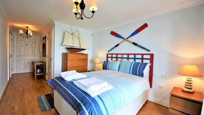 Une chambre à coucher comprenant un lit, une table de chevet, une lampe, une commode, une chaise, une petite table, une maquette de bateau et une planche de paddle fixée au mur.