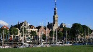 A marina with boats docked, a prominent tower, and traditional buildings in the background.
