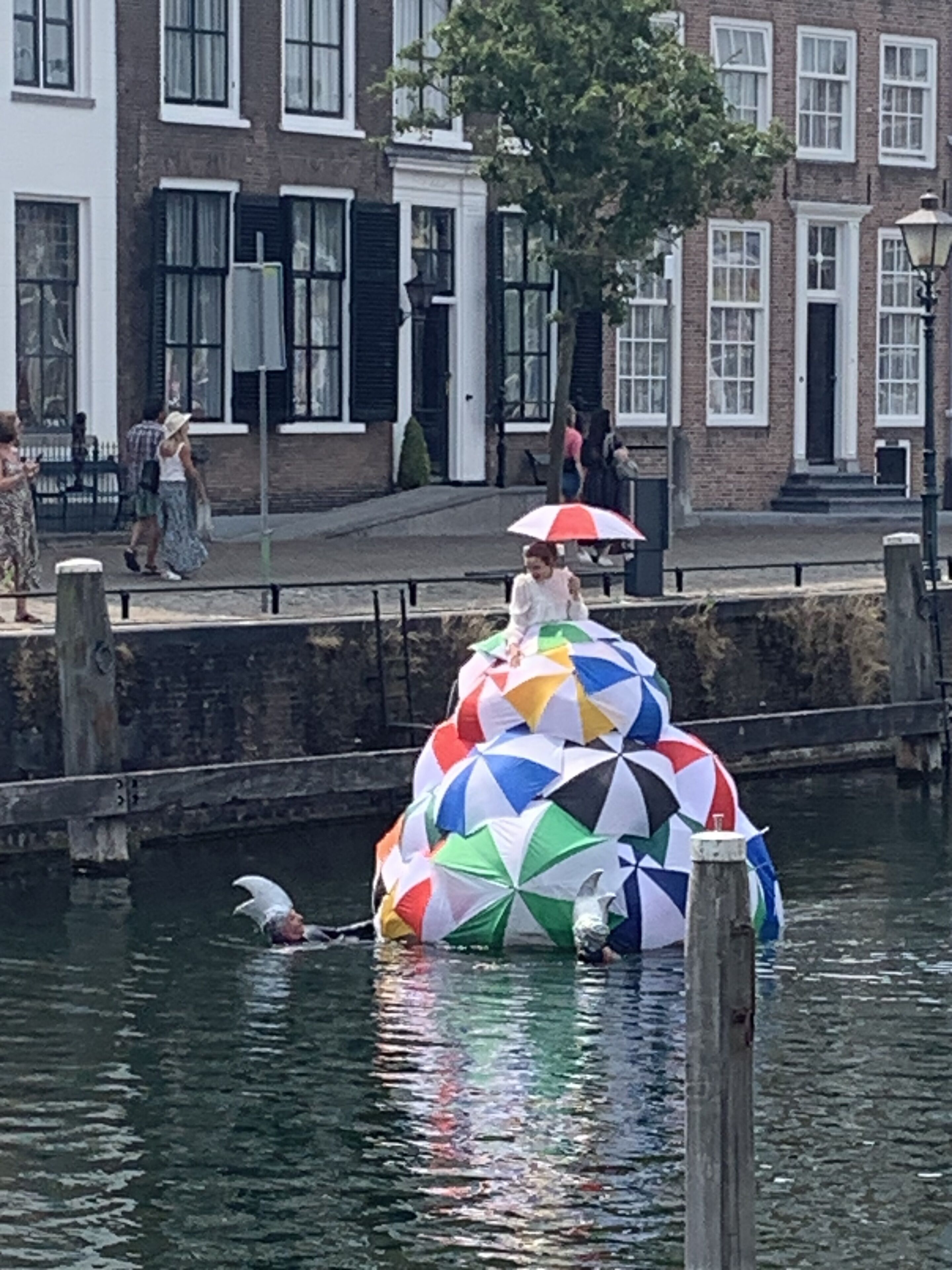 A colorful umbrella sculpture in a canal with a building in the background.