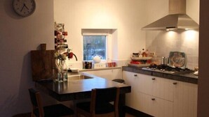 A compact kitchen with a wooden dining table, two chairs, a clock on the wall, and a window.
