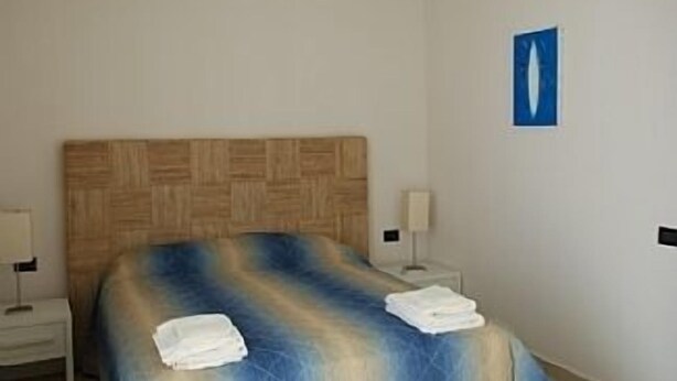 A bedroom with a wooden headboard, a bed with a blue and beige blanket, two bedside tables with lamps, and a blue wall decoration.