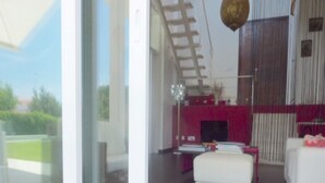 Een modern interieur met een glazen deur naar een balkon, een rode accentmuur en een witte stoel.