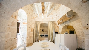 A stone-walled dining area with a white table set for four, a wooden ceiling, and a view through an archway.