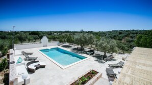 A rooftop pool area with lounge chairs, a swimming pool, and a view of the surrounding landscape.
