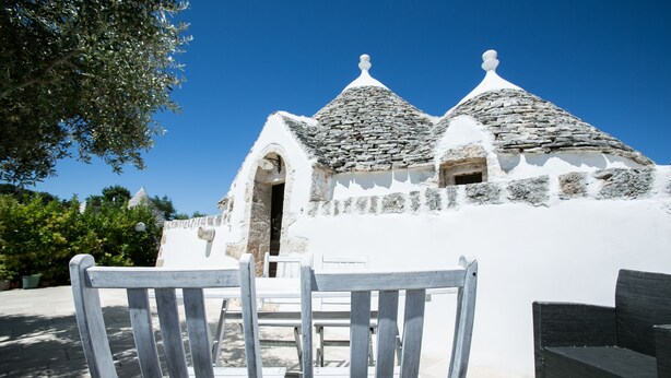A white building with stone roofs and a wooden chair in the foreground.