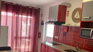 A modern kitchen with red cabinets, a stainless steel sink, and a microwave.