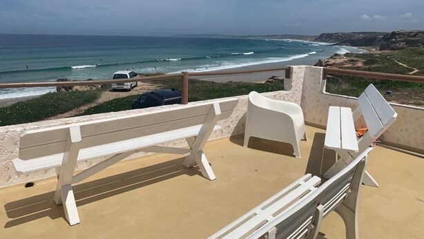 A beachside terrace with a white bench and lounge chairs, overlooking the ocean.
