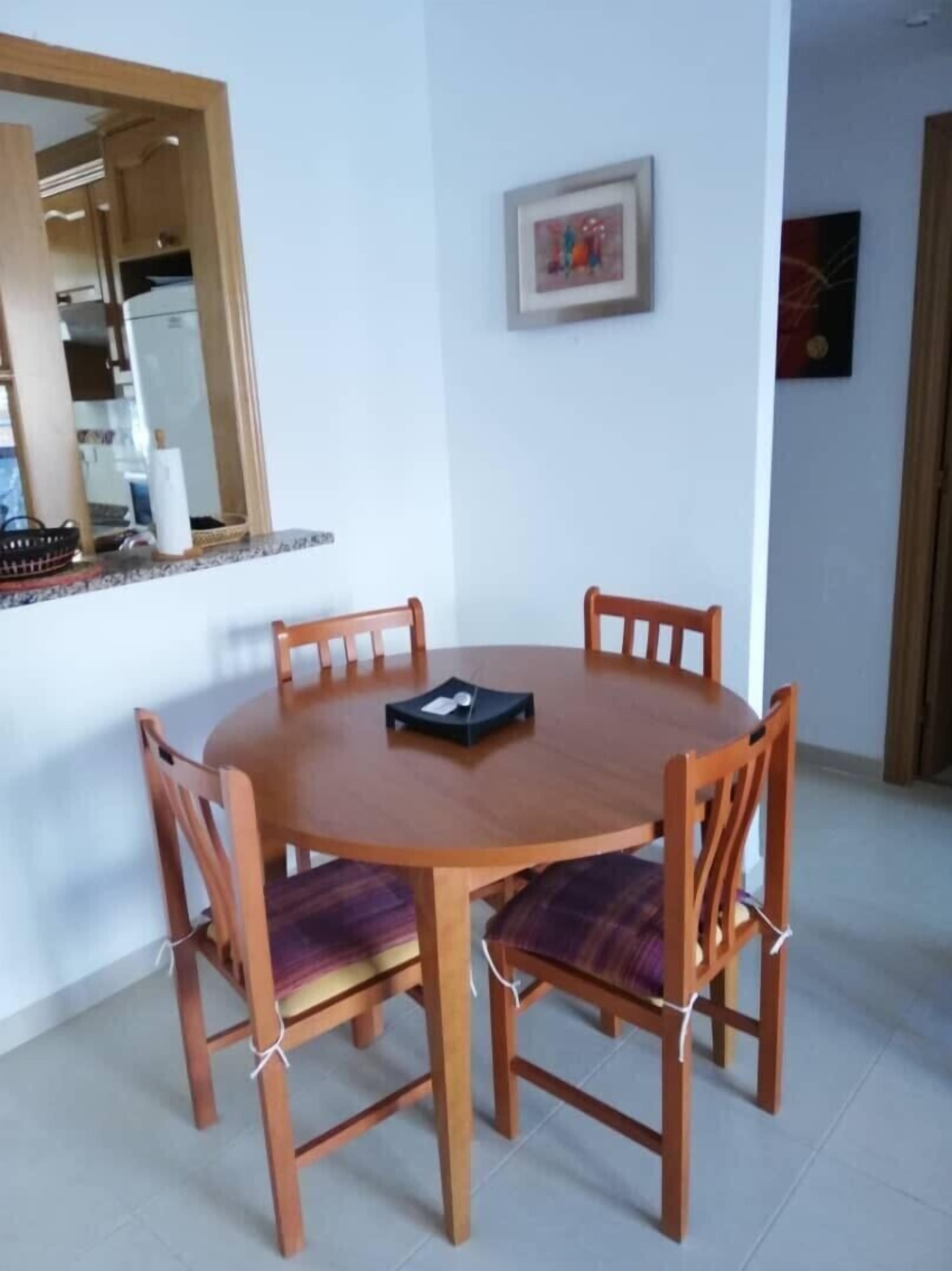 Un tavolo rotondo in legno con quattro sedie, un vassoio nero e una cornice con un'immagine appesa al muro.