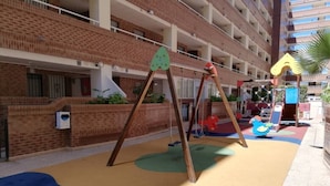 Un terrain de jeux avec des balançoires et un toboggan, entouré d’un bâtiment en briques doté de nombreux balcons.