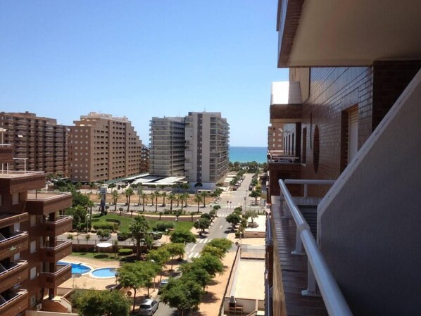 A high-rise building with multiple balconies overlooking a coastal area with palm trees and a clear blue sky.