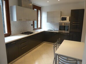 Una cocina moderna con armarios oscuros, encimera blanca, estufa a gas, horno, microondas y una mesa de comedor con sillas.