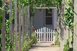 Un étroit sentier mène à une clôture blanche en bois et à un bâtiment doté d’une fenêtre.