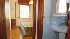 Ein Schlafzimmer mit Bett, Fenster und einem Badezimmer mit Waschbecken und Spiegel.