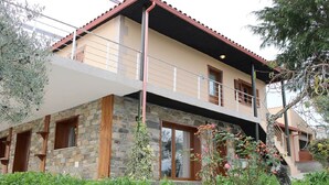 Un immeuble de deux étages avec une façade en pierre, un balcon et un toit recouvert de tuiles rouges.
