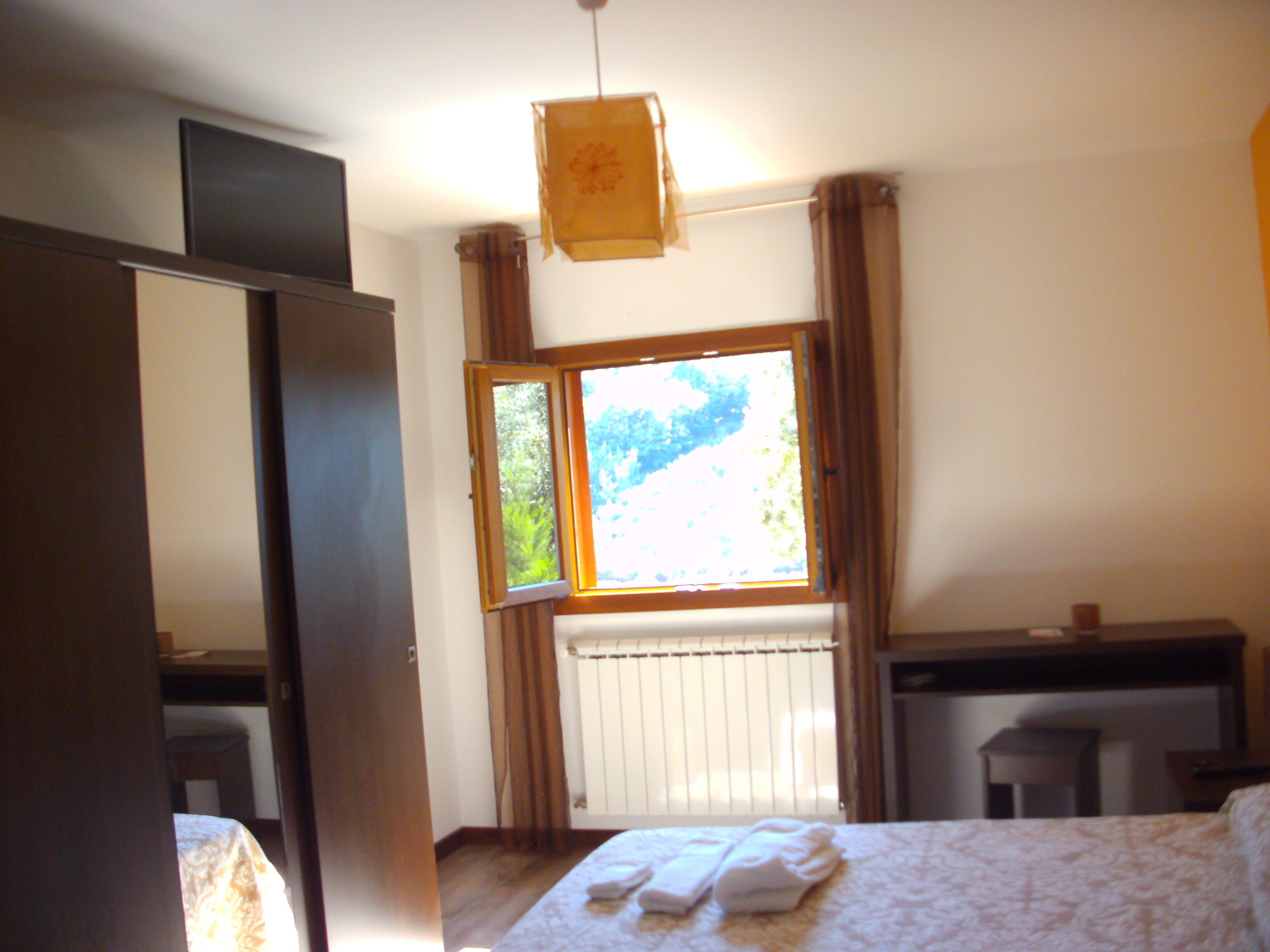 A hotel room with a bed, a desk, a radiator, and a window with curtains.