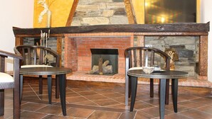 Une pièce avec une cheminée en pierre, deux fauteuils et une table.