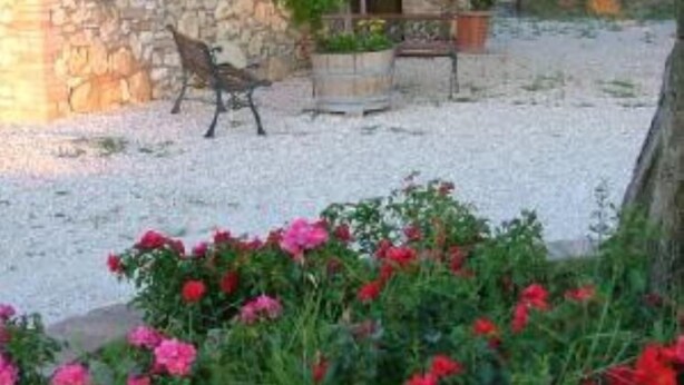 Un bâtiment en pierre avec un toit en tuiles, un banc et un jardin agrémenté de fleurs rouges.