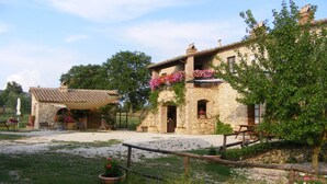 Un bâtiment en pierre avec un toit en tuiles, une clôture en bois et un chemin de gravier.