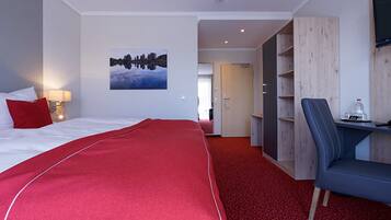 A hotel room with a bed, a desk, a chair, a TV, and a painting on the wall.