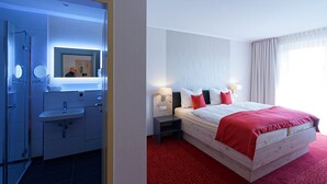 A hotel room with a large bed, a bedside table, a nightstand, a mirror, a sink, and a shower. - Hotel Stadt Magdeburg (Perleberg)